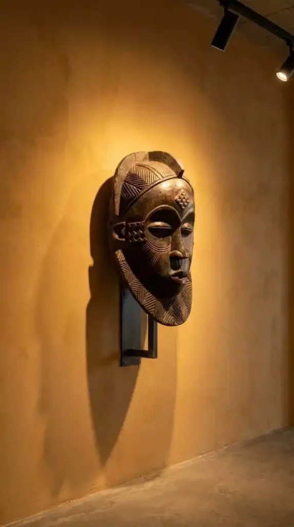 Single-carved-African-mask-mounted-alone-on-warm-ochre-plaster-wall