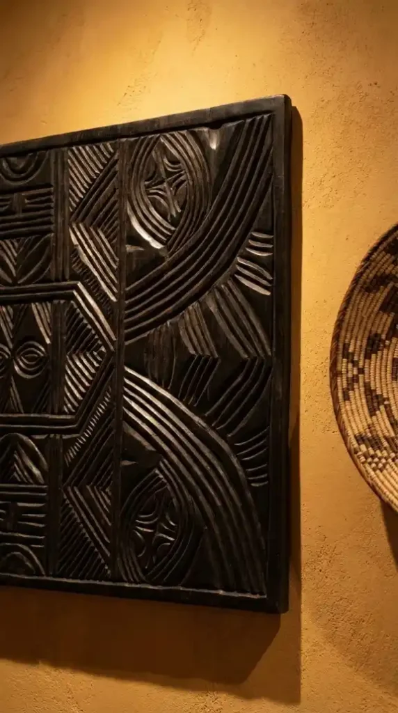 Carved-dark-ebony-wood-relief-panel-catching-warm-track-light-shadows