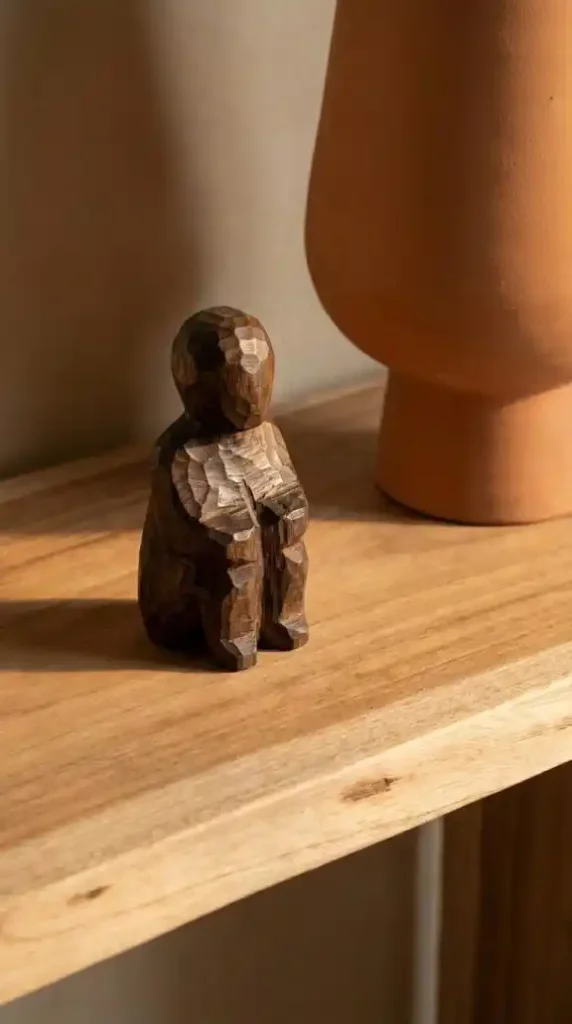 close-up-of-a-small-hand-carved-dark-mango-wood-figurine-on-a-raw-wood-console-surface