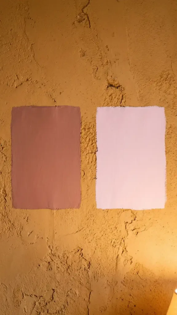 close-up-of-two-paint-swatches-held-against-a-warm-ochre-plaster-wall