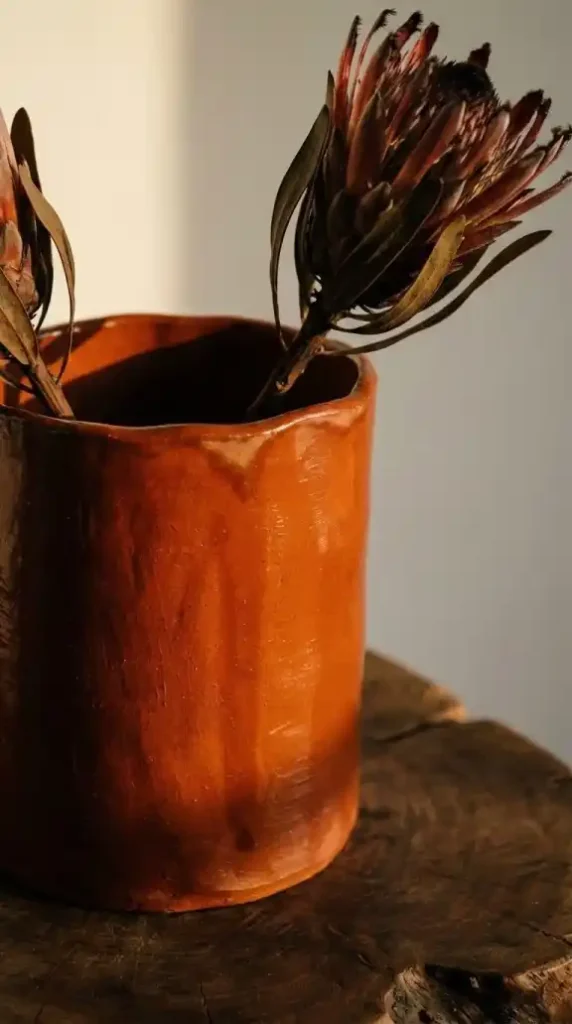 hand-thrown-terracotta-vessel-in-deep-burnt-orange-slightly-irregular-rim-visible-positioned-on-a-raw-dark-wood-surface