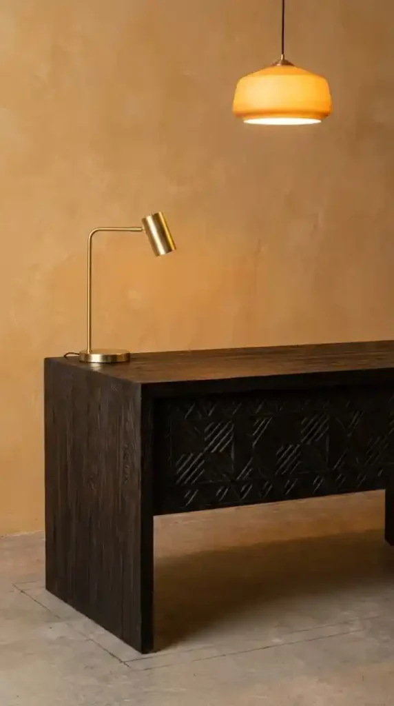 Reclaimed-dark-ebony-desk-with-brass-lamp-against-warm-ochre-plaster